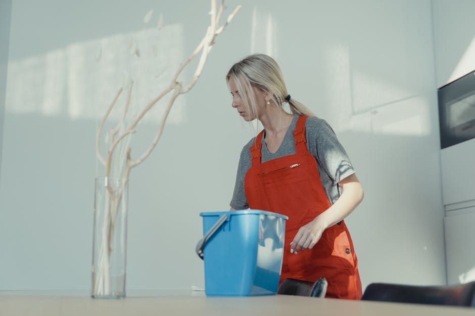 A person wearing a light green cleaning glove is seen reaching for or organizing a set of white books or magazines on a dark wooden shelf in a domestic setting. The shelf appears to be part of a livin